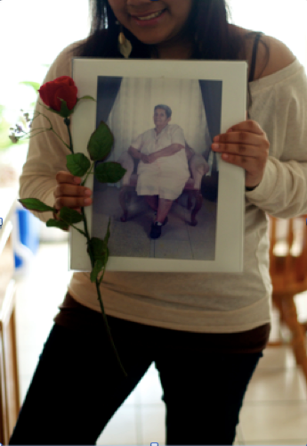 A teen girl holds a photograph of her grandmother and a rose.